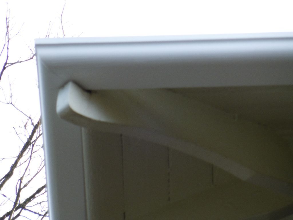 White house eave corner with a decorative bracket, against a cloudy sky.