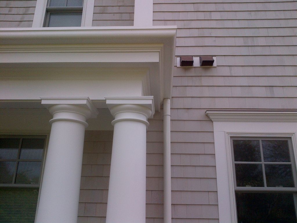 White columns supporting a porch roof with windows. Two vents on weathered gray siding.