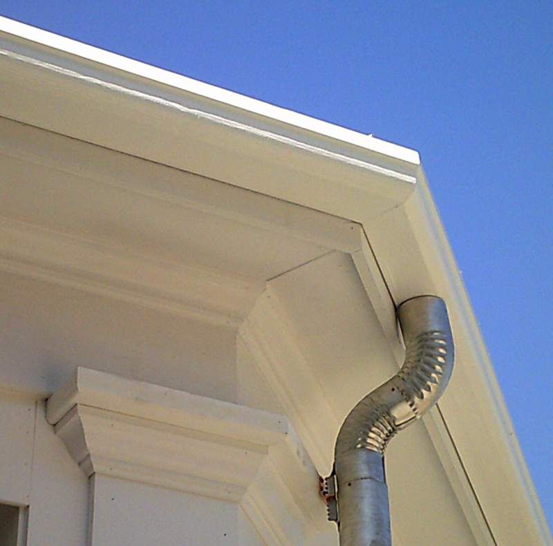 White building corner with gutter and downspout against blue sky.