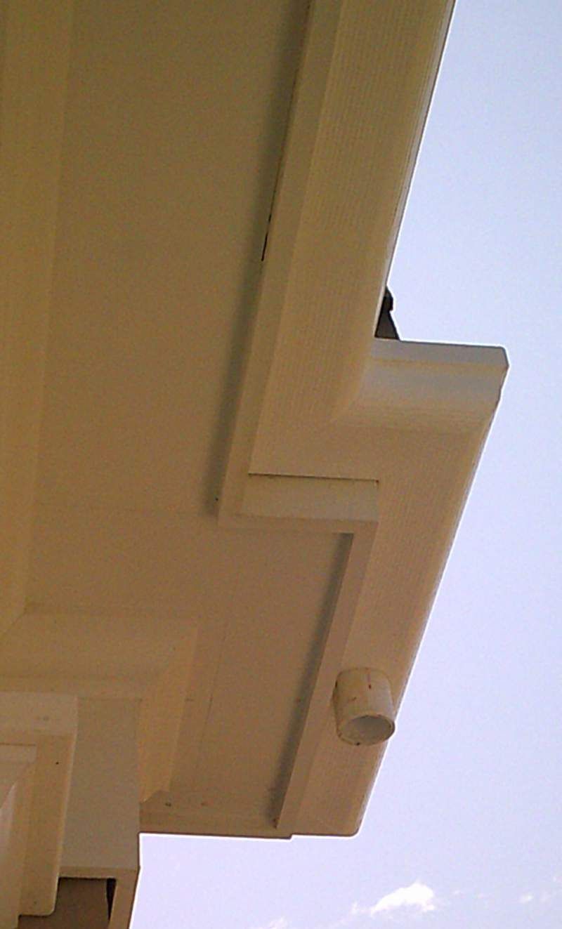 Off-white building overhang with gutter and downspout against a pale blue sky.