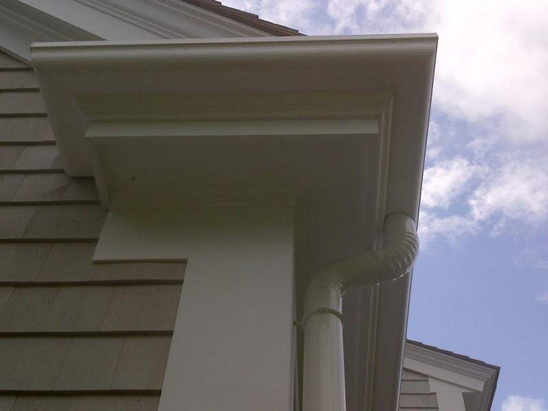 White house corner with rain gutter and downspout against a cloudy sky.