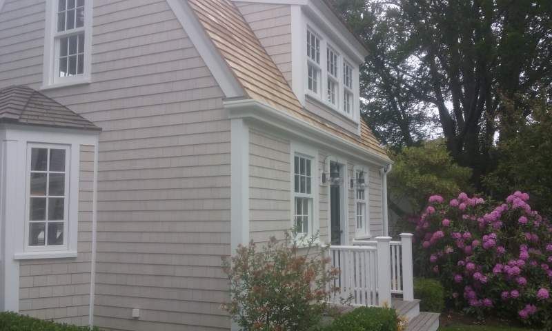 Light-colored house with white trim, windows, and small porch. A flowering bush sits in front of the house.
