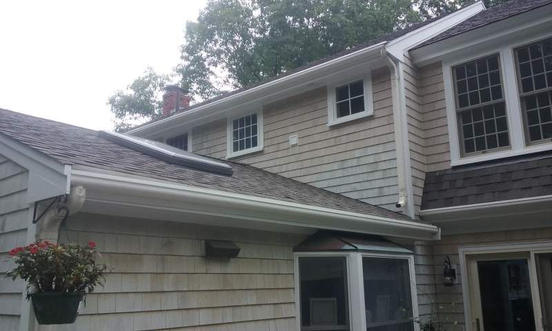 House exterior with light siding, white trim, and a dark shingled roof; Gutters and windows are visible.