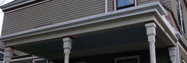 A light-colored porch with white columns is attached to a house with a gray exterior.