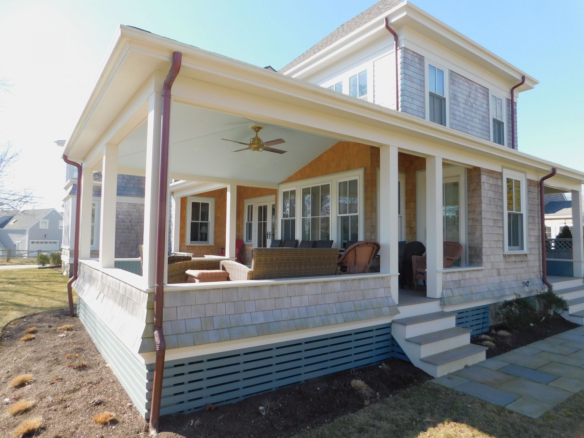 Covered porch of a house with light blue ceiling, stone steps, cedar shingle siding, and grass yard.