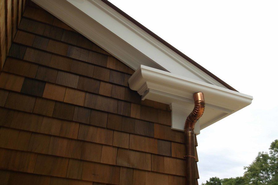 Brown shingle siding with white trim and a copper rain gutter on a house.