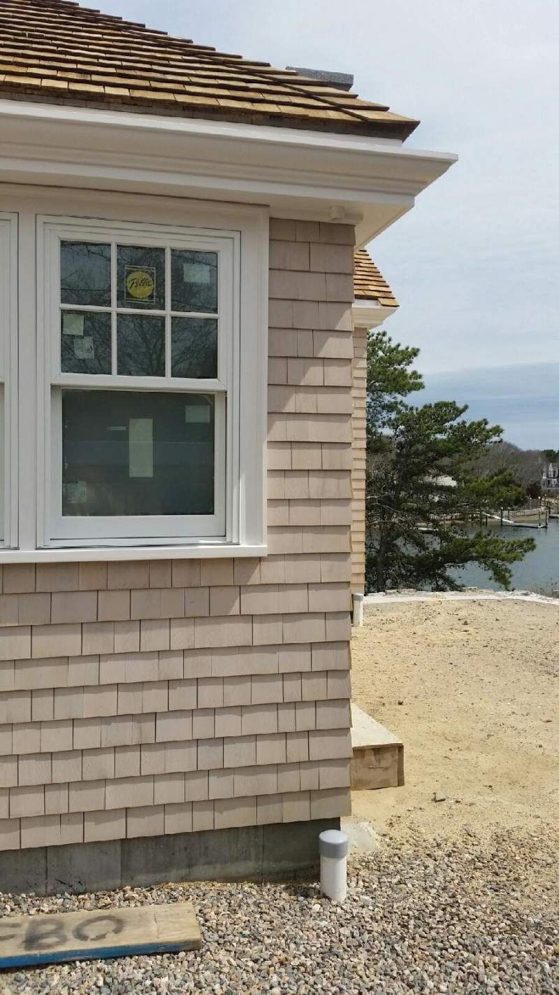 Exterior of a building with cedar shake siding, a window, and a roof, near water.