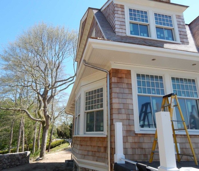 Exterior of a house under construction with brown cedar shingles and white trim. A ladder is present.