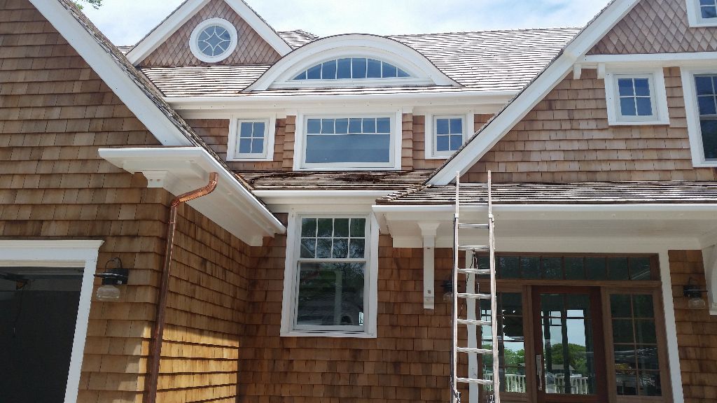 Brown shingle house with white trim, various windows, and a ladder leaning against the front.
