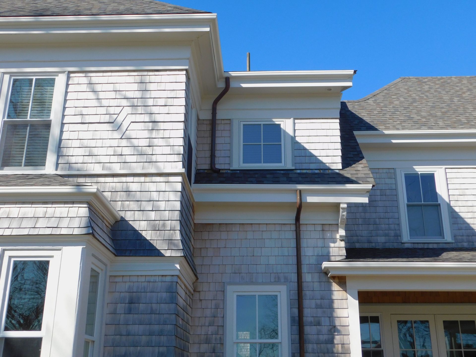Gray shingle-clad house with white trim, windows, and gutters against a blue sky.