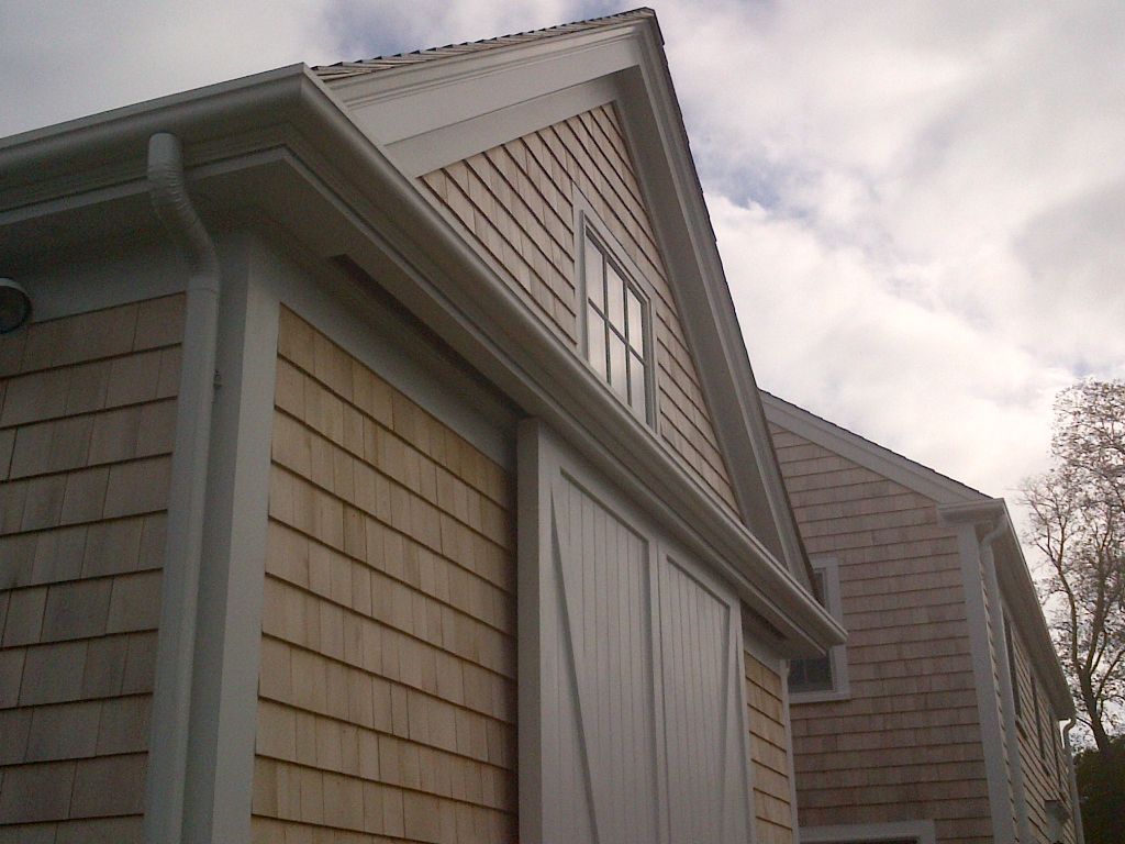 Light wood shingle siding on a building with a white trim and a white sliding door.