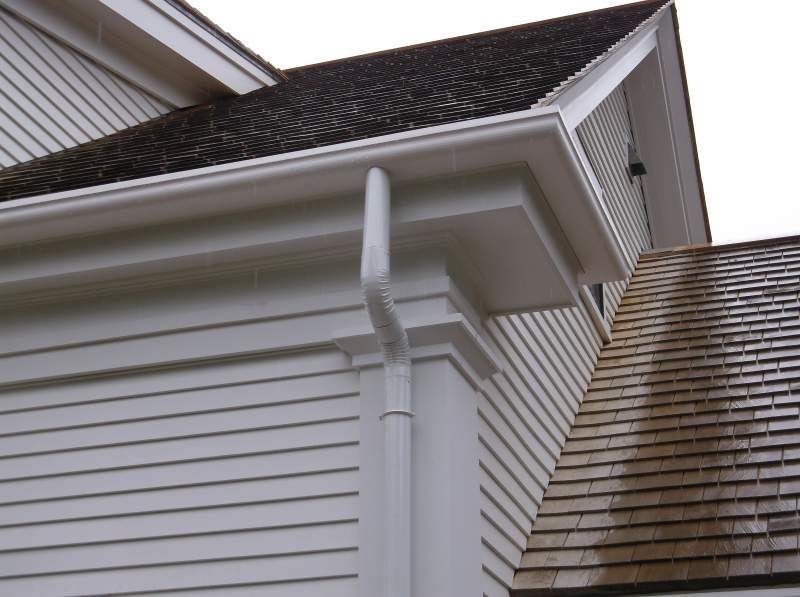 White siding and gutters on a building with a dark roof.