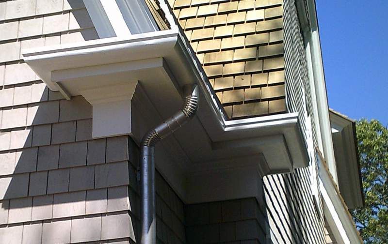 Exterior house corner with gray shingles, white trim, and a silver gutter.