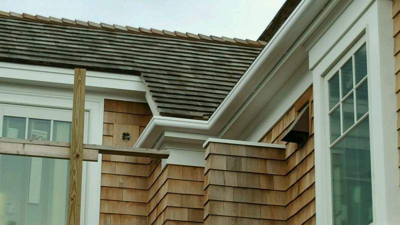 Exterior of a house with cedar shake siding, white trim, and a gutter, on a cloudy day.