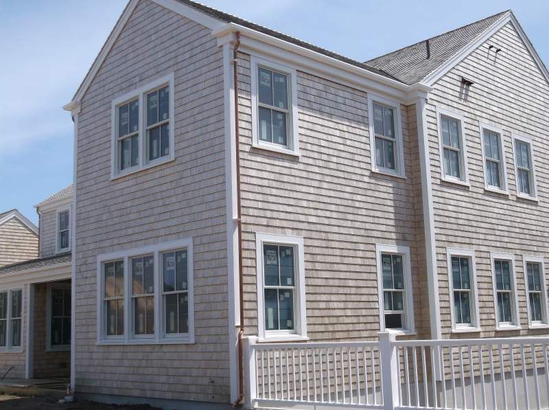 Two-story house with cedar shingle siding and white-framed windows, behind a white picket fence.