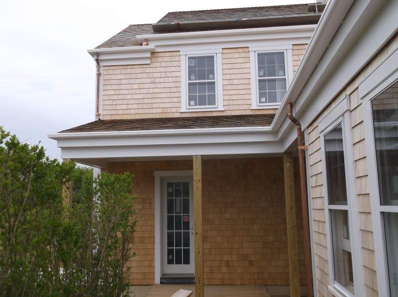 Two-story building with light brown cedar shingles, white trim, copper gutters, and windows.
