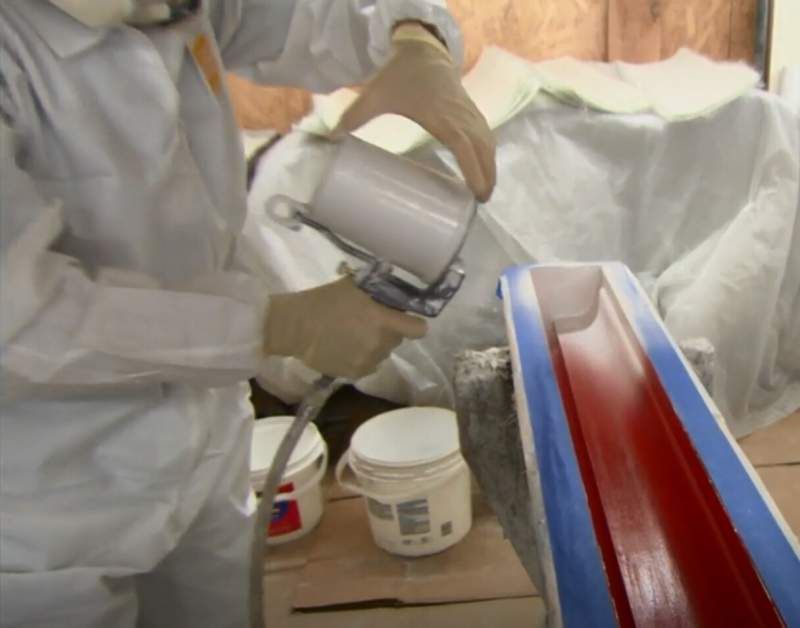 Person in protective gear spraying white paint onto a red-lined mold.