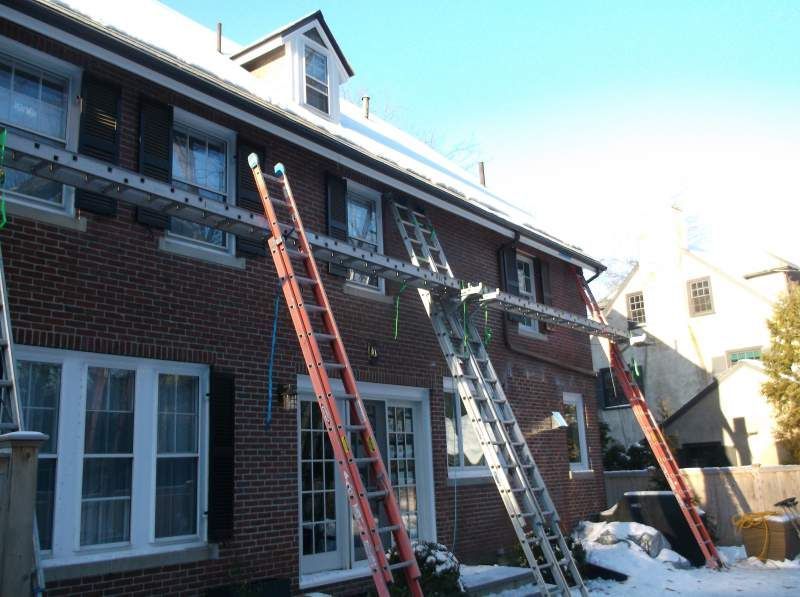Ladders propped against a brick house with snow on the roof; metal scaffolding spans across the wall.