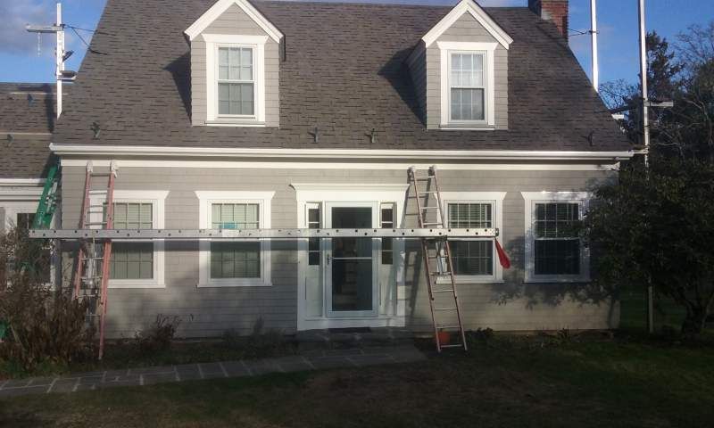 Gray house exterior with two dormers, multiple windows, and ladders.