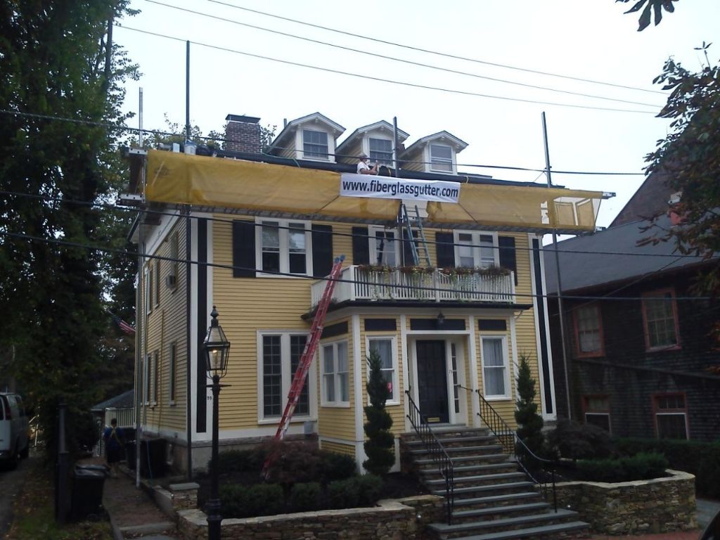Yellow house with construction netting around the roof, scaffolding, and a ladder leaning against it.