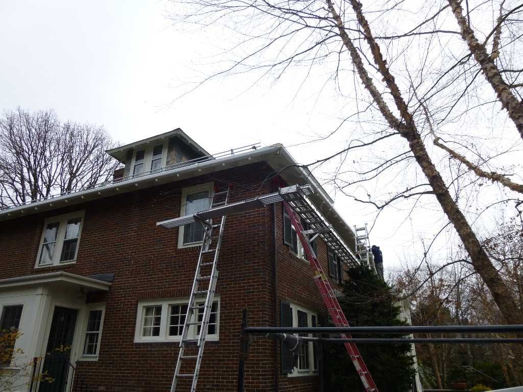 A brick house with ladders set up against it for gutter cleaning or repair, cloudy sky overhead.