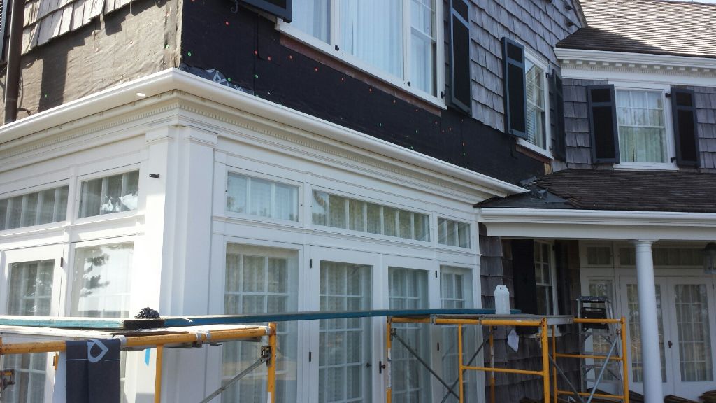 Exterior of a house under construction; white trim, dark siding, scaffolding, windows.