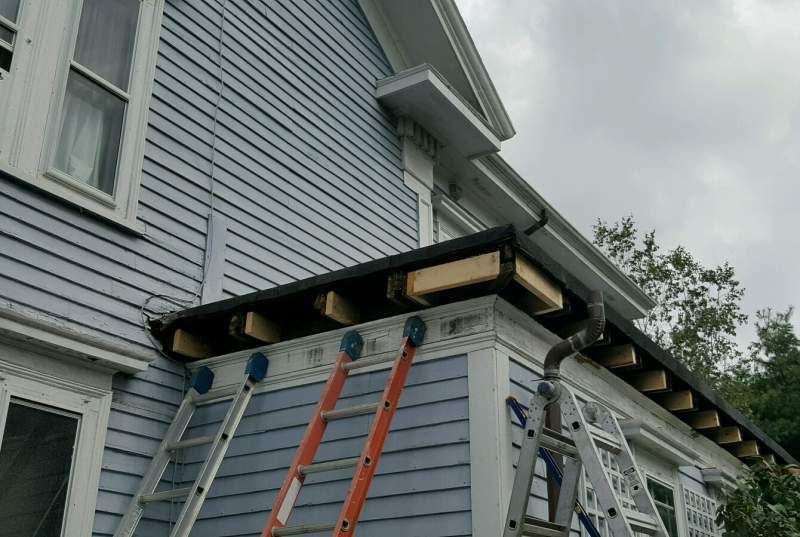 House exterior with blue siding, roof repair in progress, ladders propped against the building.