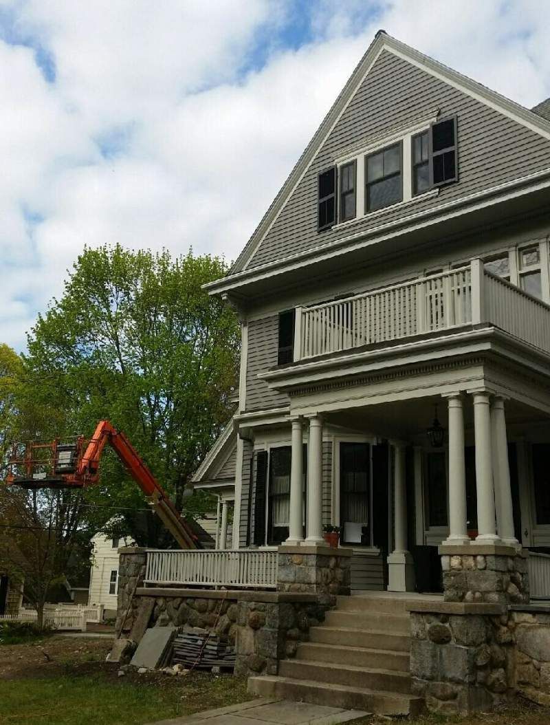 Gray house with a porch and steps; a lift in the yard, likely for renovations.