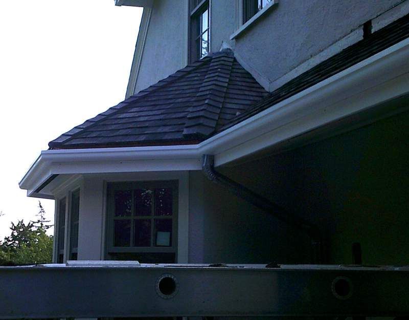 White guttering on a building with dark gray shingles and a window.