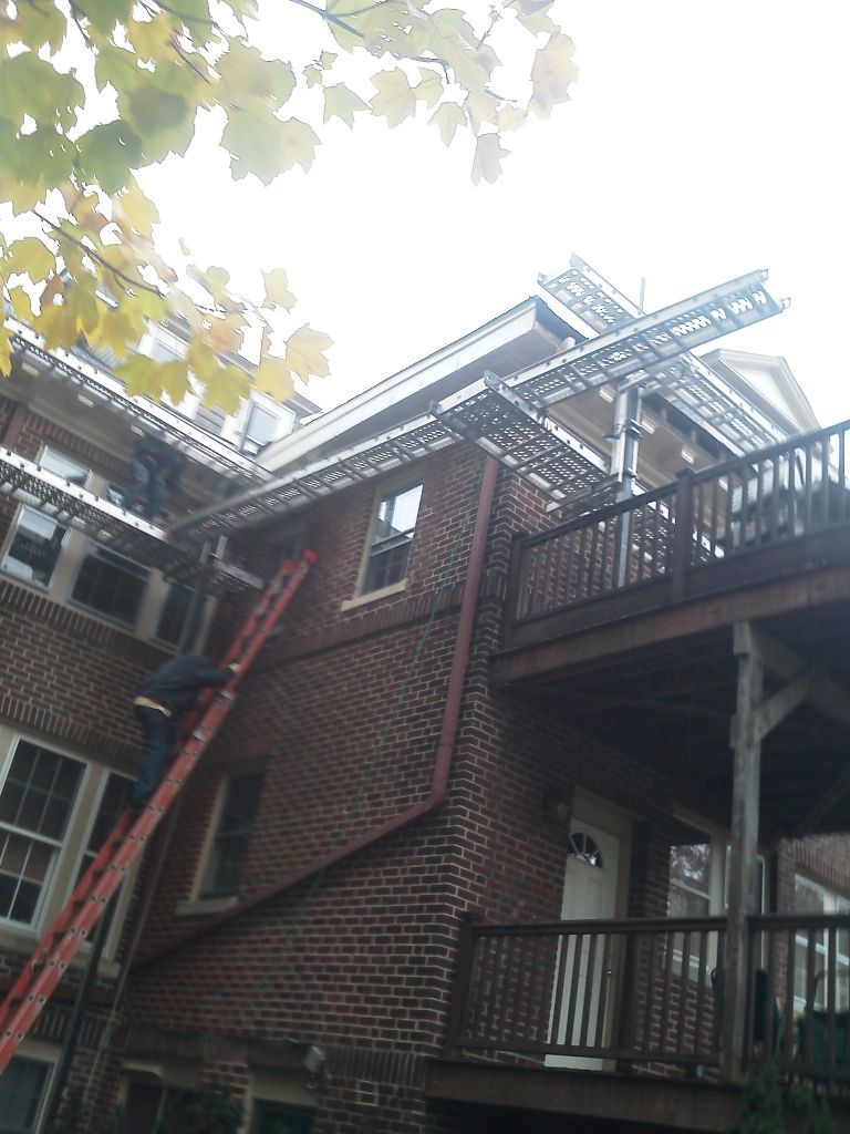 Workers installing gutters on a brick building, using ladders and scaffolding.