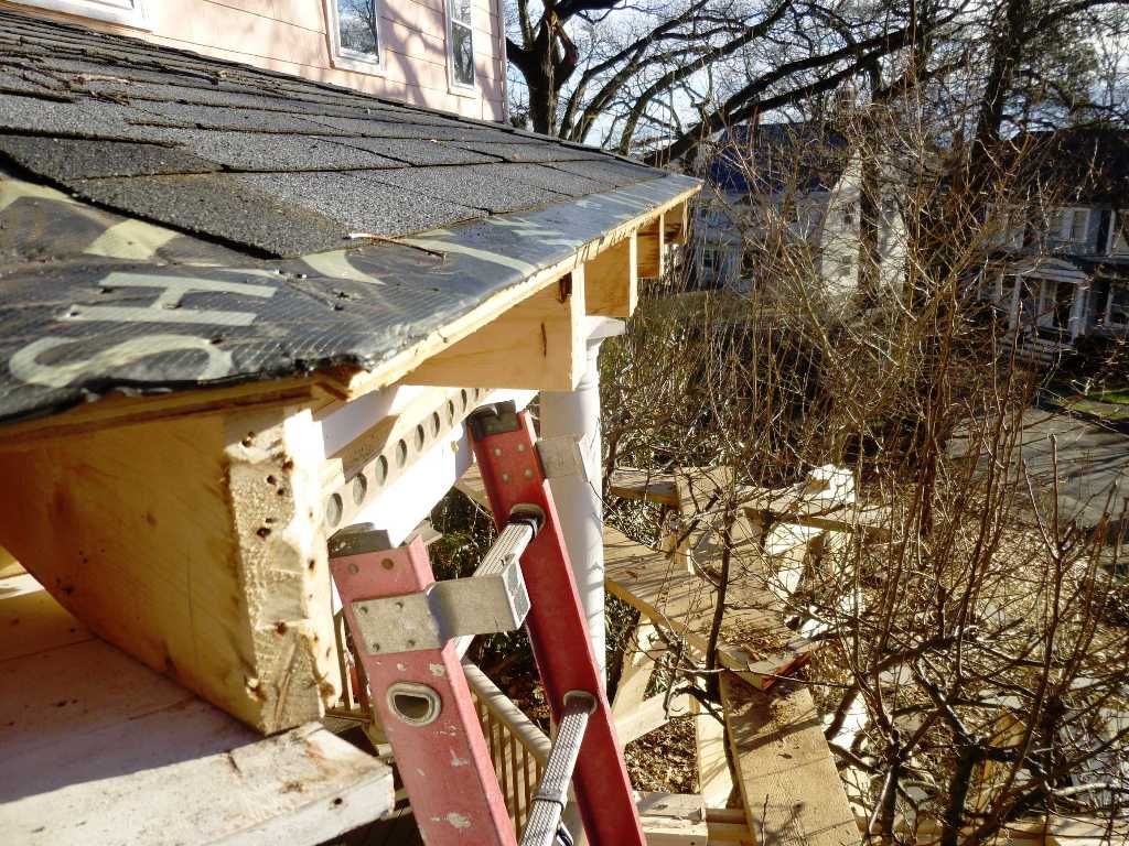 Construction site with a partially built porch roof, ladder leaning against it.