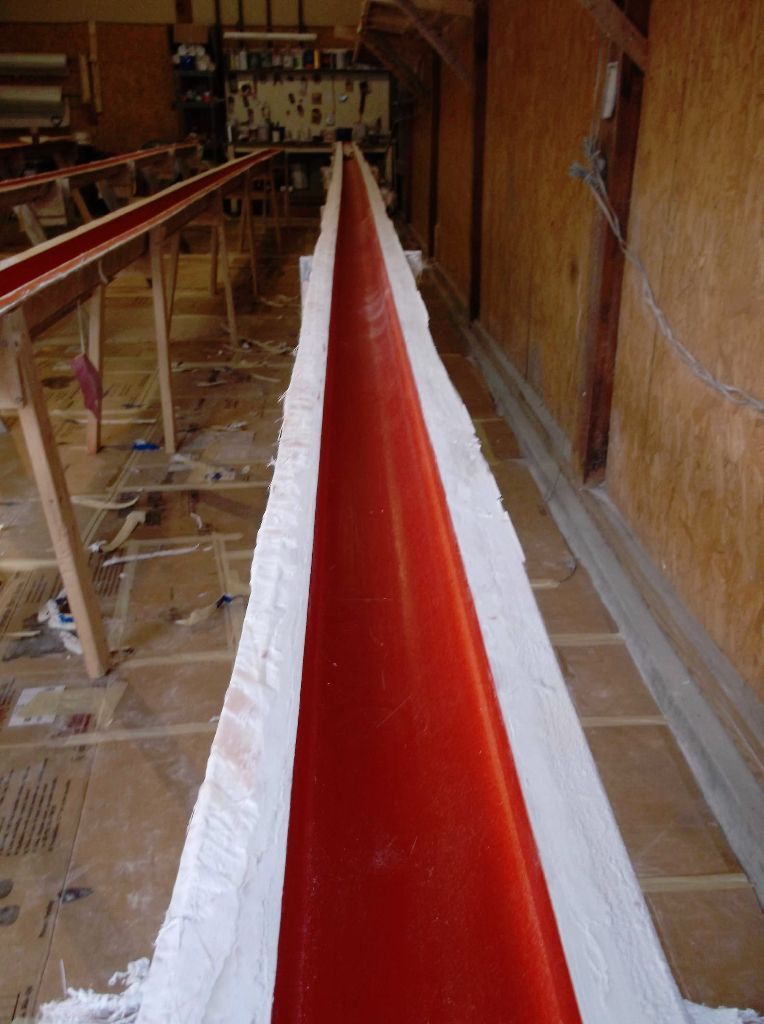 Long, red channel in a white mold, on a wooden floor in a workshop.