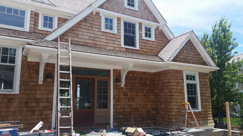 Brown shingled house under construction with white trim, windows, and a ladder.