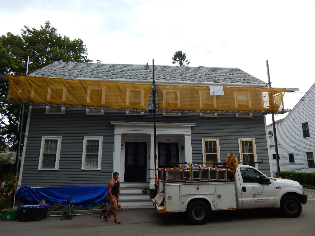 A gray house under construction, with a truck in front and a person walking by.