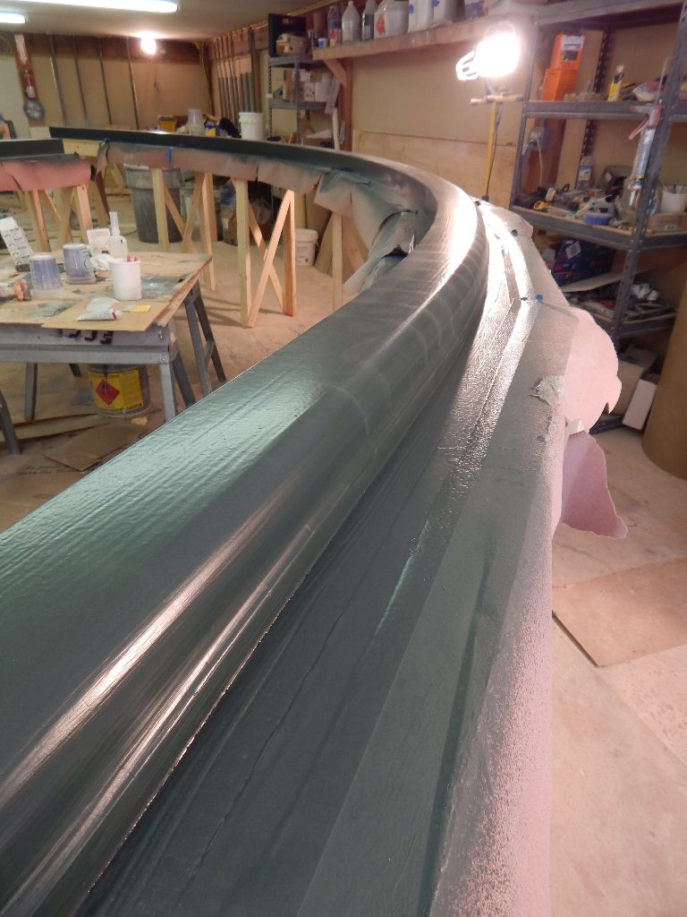 Curved, dark gray structure in a workshop; likely a model or form, with tools and materials visible.