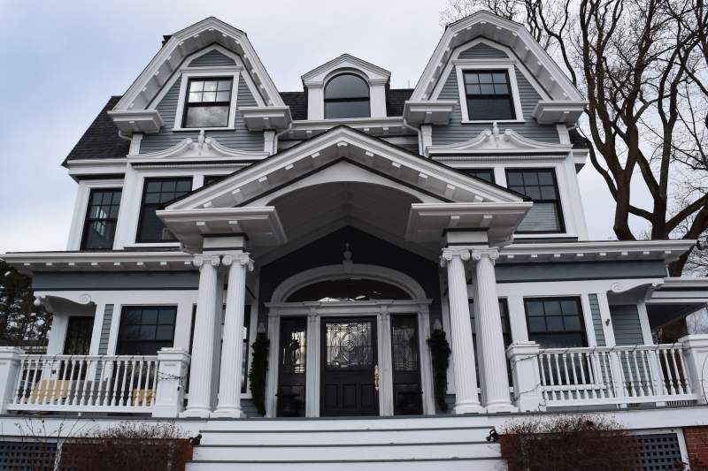 Grey Victorian house with white trim, porch, and columns. Two dormers and a dark front door.