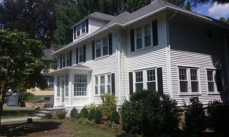 Two-story white house with black shutters and a small garden in front.