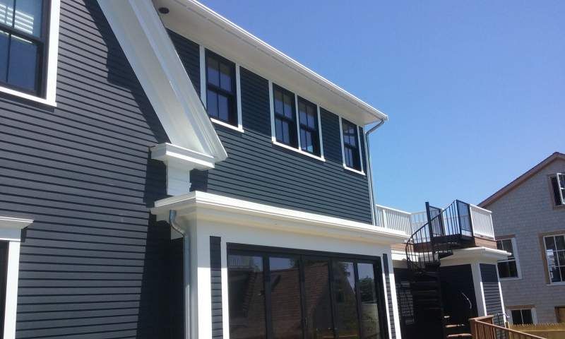 Blue-sided house with white trim and dark windows. A spiral staircase and sunny blue sky are in the background.