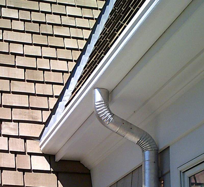 Guttering and downspout on a white fascia board, attached to a house with brown shake siding.