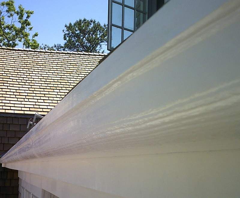 White house trim detail with a shingled roof in the background and a blue sky.