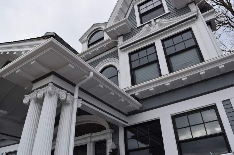 Gray and white Victorian house with ornate architectural details, viewed from a low angle on an overcast day.