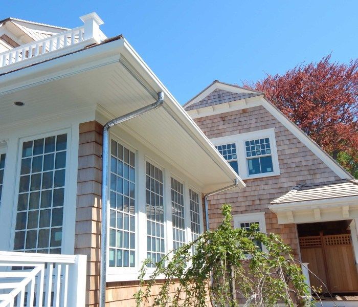 A light-colored house with many windows and shingle siding has a bright blue sky background.