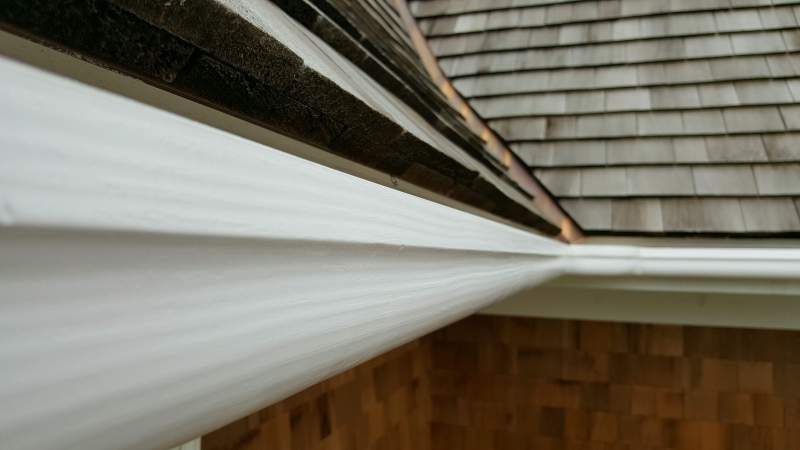 White rain gutter attached to a cedar shake roof.