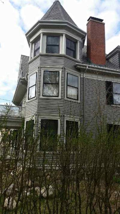 Gray Victorian house with turret and red brick chimney.