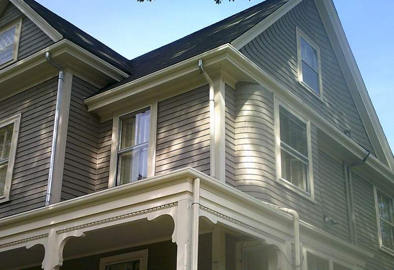 Two-story house with gray siding, white trim, and a dark roof under a blue sky.