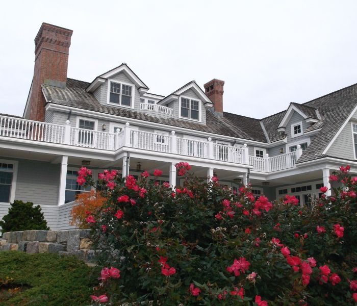 Large gray house with white trim, red brick chimneys, and a balcony; red roses in front.
