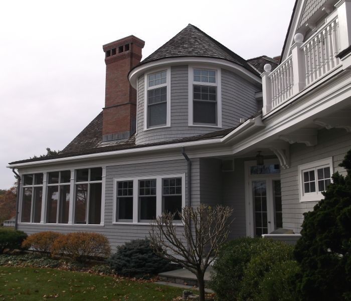 Gray house with a rounded turret and a red brick chimney on an overcast day.