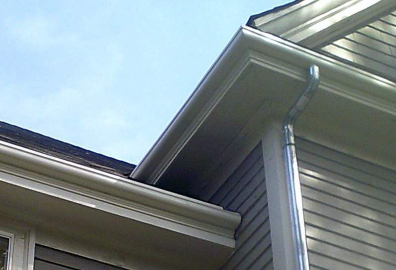 Beige gutters and downspout on a light-colored house, against a blue sky.