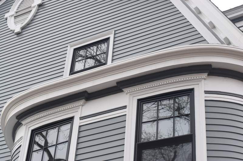 Gray house exterior with white trim, black windows, and curved roofline detail.