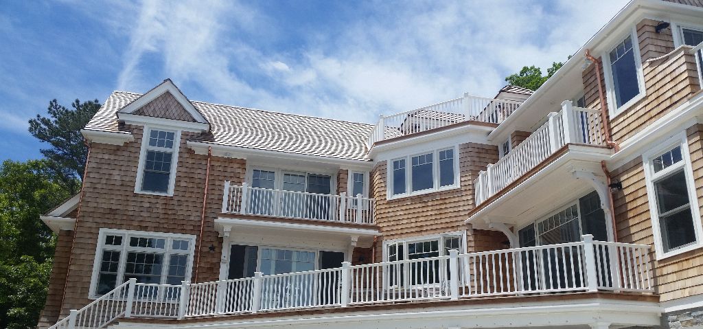 Multi-story house with cedar shake siding, white balconies, and a blue sky background.